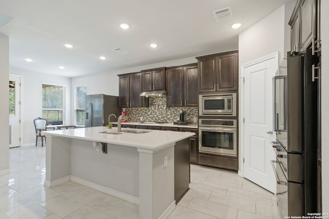 kitchen with sink, stainless steel appliances, backsplash, an island with sink, and dark brown cabinets