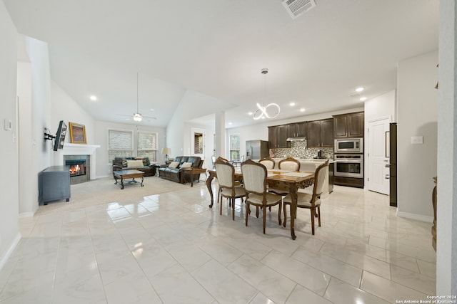 tiled dining space with ceiling fan with notable chandelier and lofted ceiling