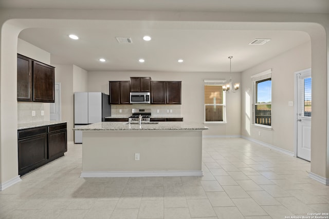 kitchen featuring light stone counters, a kitchen island with sink, appliances with stainless steel finishes, and tasteful backsplash