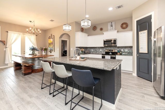 kitchen featuring light hardwood / wood-style floors, hanging light fixtures, appliances with stainless steel finishes, light stone counters, and tasteful backsplash