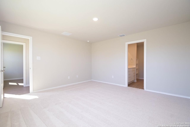 unfurnished bedroom with ensuite bathroom and light colored carpet