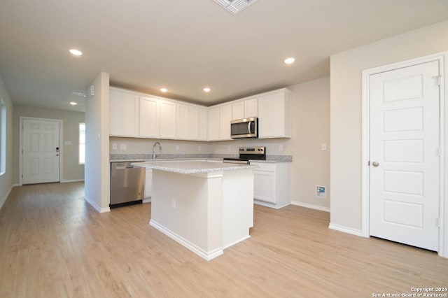 kitchen featuring appliances with stainless steel finishes, light stone counters, a kitchen island, light hardwood / wood-style flooring, and white cabinetry