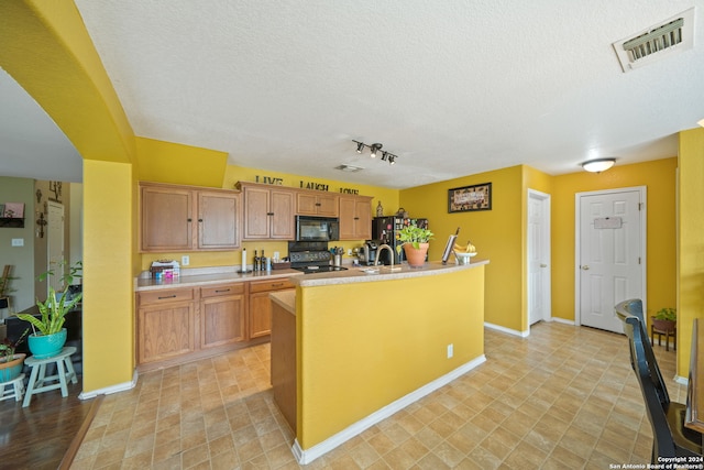 kitchen featuring a textured ceiling, black appliances, a kitchen island with sink, track lighting, and light tile flooring