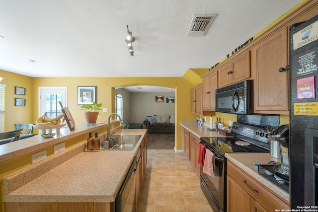 kitchen featuring a kitchen island with sink, black appliances, track lighting, sink, and a textured ceiling