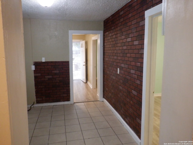 hall with light tile patterned floors, a textured ceiling, and brick wall