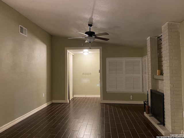 unfurnished living room with a textured ceiling, vaulted ceiling, ceiling fan, dark wood-type flooring, and a fireplace