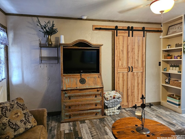 interior space with a barn door, ceiling fan, hardwood / wood-style flooring, and ornamental molding