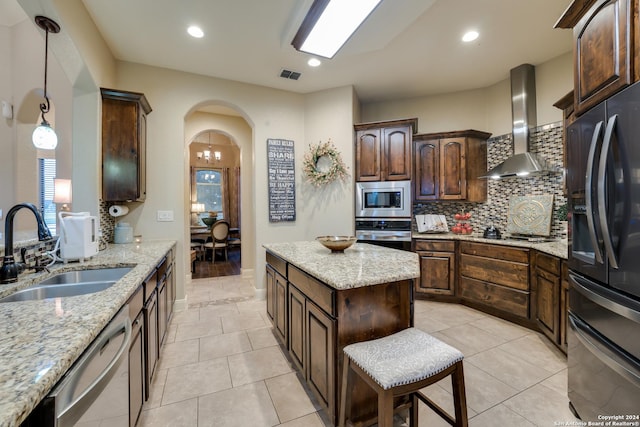 kitchen featuring backsplash, wall chimney range hood, sink, light stone counters, and stainless steel appliances