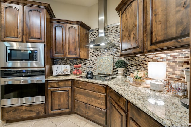 kitchen with decorative backsplash, light stone counters, wall chimney range hood, stainless steel microwave, and black stovetop