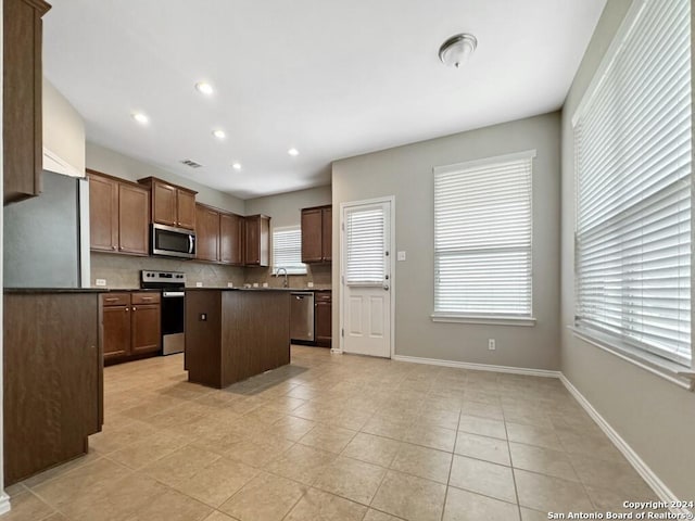 kitchen with appliances with stainless steel finishes, a center island, a wealth of natural light, and backsplash