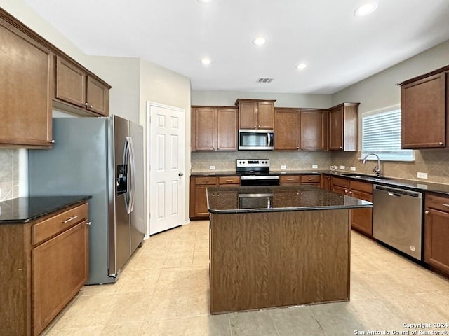 kitchen featuring appliances with stainless steel finishes, tasteful backsplash, sink, dark stone countertops, and a kitchen island