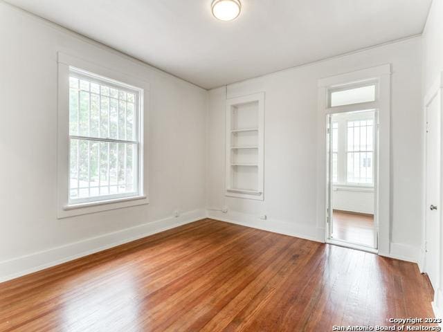 spare room with built in shelves and hardwood / wood-style flooring