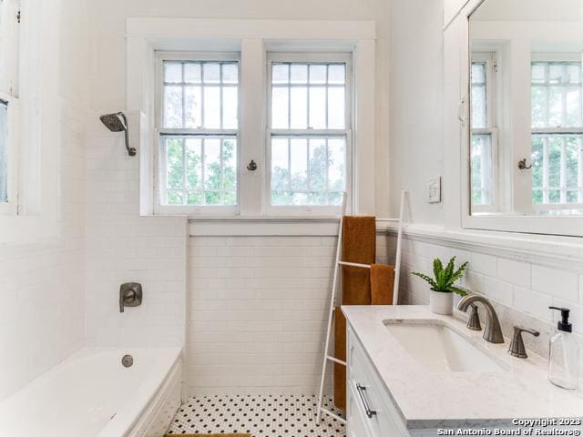 bathroom with vanity, tiled shower / bath combo, and tile walls