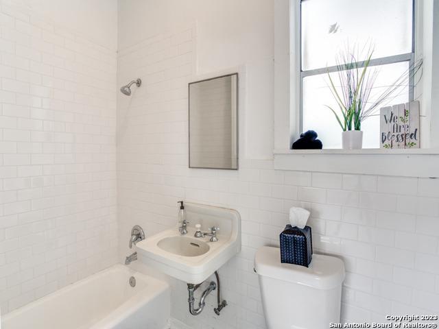 bathroom featuring toilet, a bath, and tile walls