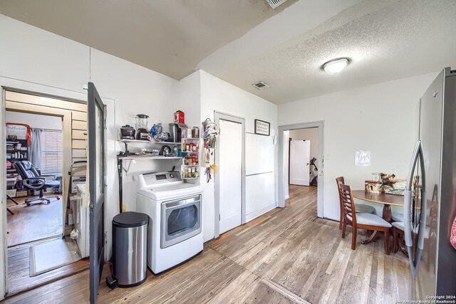 kitchen featuring hardwood / wood-style floors, range with electric cooktop, stainless steel refrigerator with ice dispenser, a textured ceiling, and washer / clothes dryer