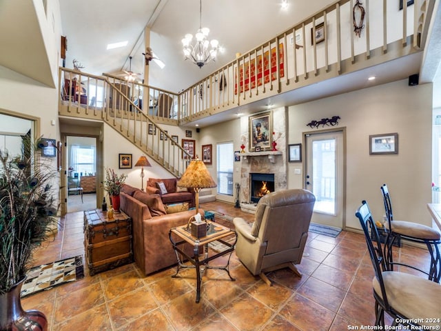 living room featuring baseboards, a towering ceiling, stairs, a fireplace, and ceiling fan with notable chandelier