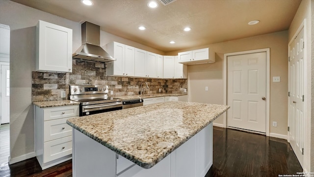 kitchen with wall chimney range hood, a kitchen island, light stone counters, white cabinetry, and stainless steel appliances