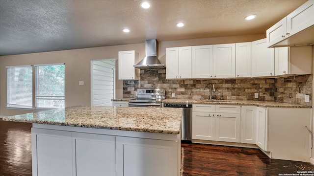 kitchen with light stone countertops, stainless steel appliances, white cabinetry, and wall chimney range hood