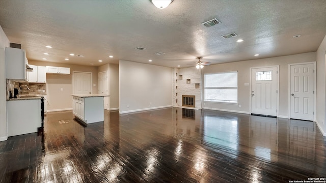 unfurnished living room with a brick fireplace, a textured ceiling, ceiling fan, sink, and dark hardwood / wood-style floors