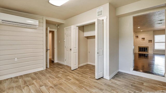 interior space featuring a wall mounted AC, a closet, light hardwood / wood-style floors, and a brick fireplace