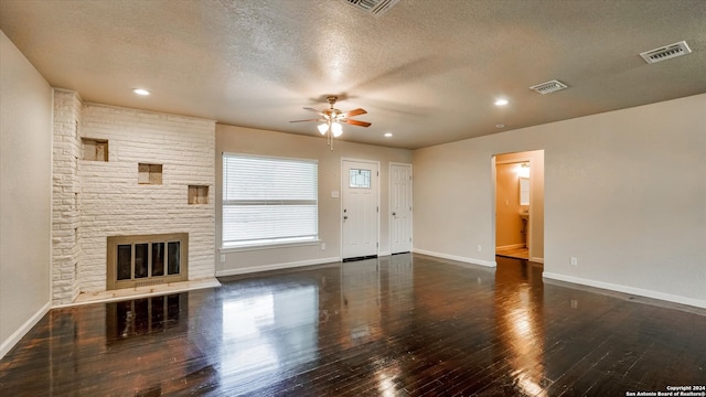 unfurnished living room with ceiling fan, a large fireplace, a textured ceiling, and dark wood-type flooring