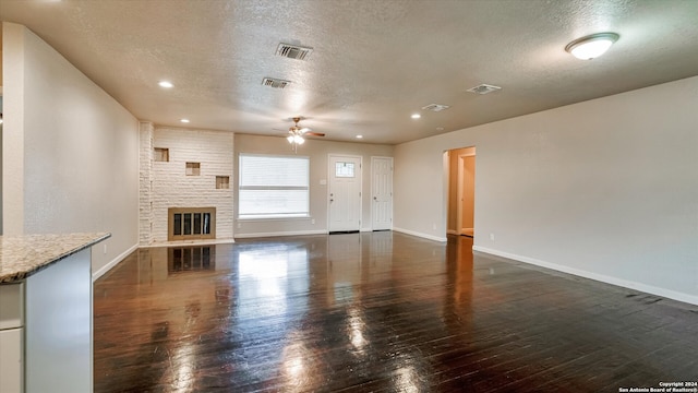 unfurnished living room with ceiling fan, dark wood-type flooring, a textured ceiling, and a brick fireplace