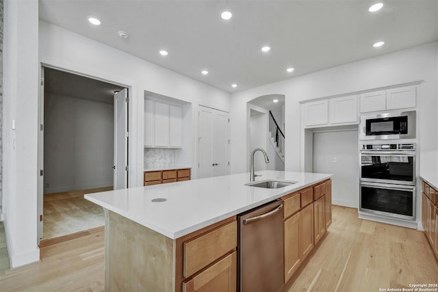 kitchen featuring white cabinetry, sink, a center island with sink, appliances with stainless steel finishes, and light wood-type flooring