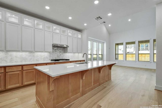 kitchen featuring lofted ceiling, a large island with sink, white cabinets, sink, and light hardwood / wood-style floors