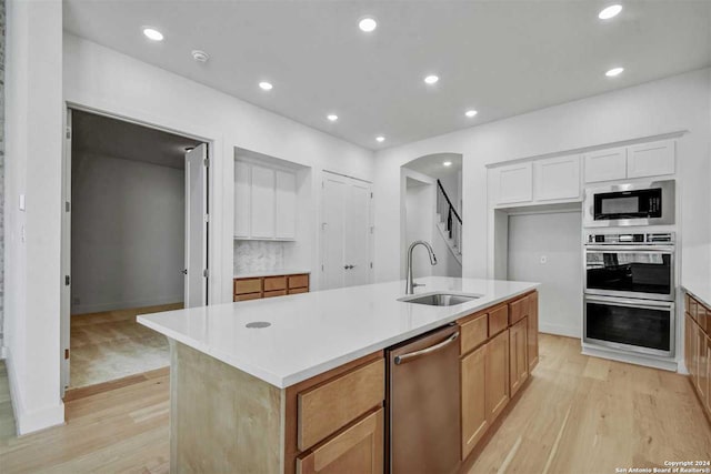 kitchen with sink, light hardwood / wood-style floors, a center island with sink, white cabinets, and appliances with stainless steel finishes