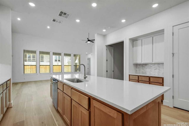 kitchen with ceiling fan, sink, backsplash, a kitchen island with sink, and light wood-type flooring