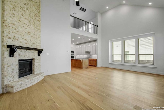 unfurnished living room with a large fireplace, ceiling fan, light hardwood / wood-style flooring, and high vaulted ceiling