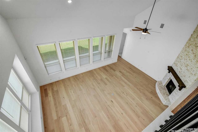 unfurnished living room featuring ceiling fan, a stone fireplace, light wood-type flooring, and high vaulted ceiling