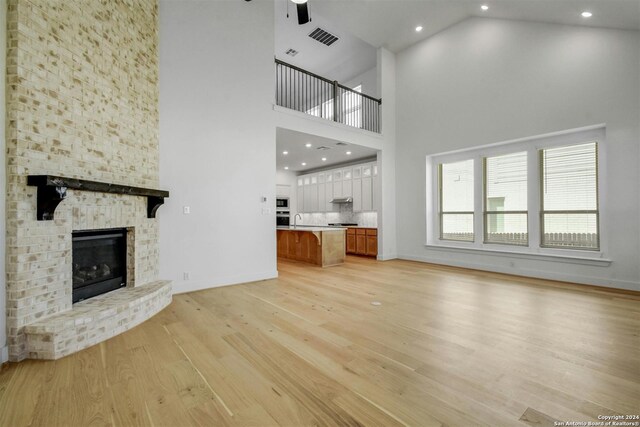 unfurnished living room featuring a large fireplace, ceiling fan, light hardwood / wood-style floors, and high vaulted ceiling