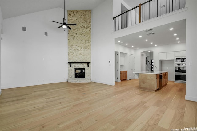 kitchen featuring high vaulted ceiling, light hardwood / wood-style floors, a center island with sink, white cabinets, and appliances with stainless steel finishes