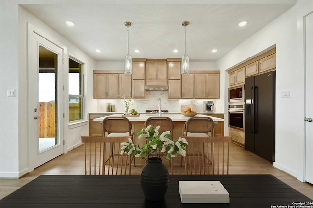 kitchen with plenty of natural light, a kitchen island with sink, stainless steel appliances, and decorative light fixtures