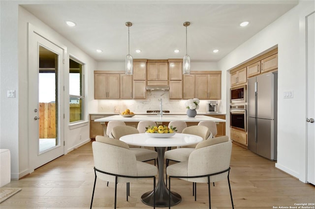 kitchen with tasteful backsplash, light hardwood / wood-style flooring, pendant lighting, a center island with sink, and appliances with stainless steel finishes