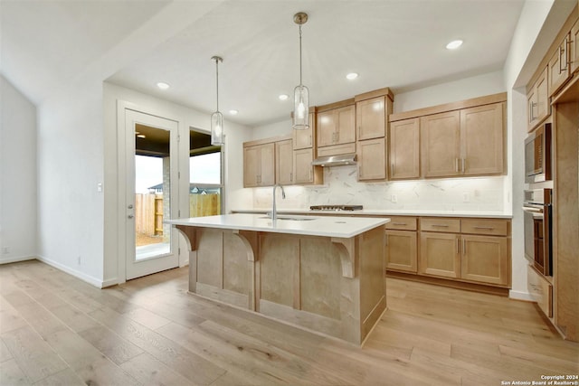 kitchen featuring light wood-type flooring, stainless steel appliances, hanging light fixtures, and a center island with sink