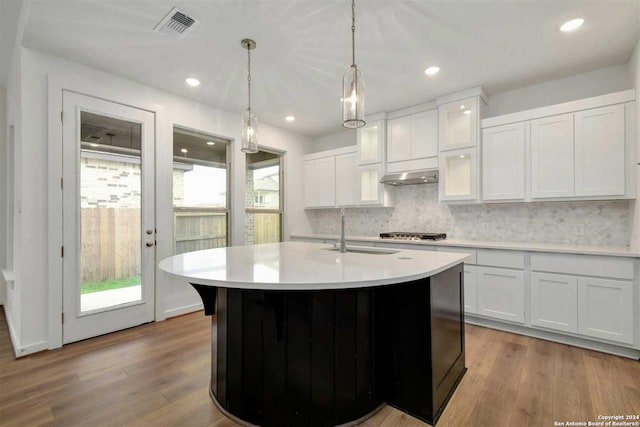 kitchen with an island with sink, range hood, white cabinetry, and sink