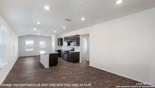 kitchen with lofted ceiling, range with gas cooktop, dark brown cabinets, a center island with sink, and dark hardwood / wood-style flooring