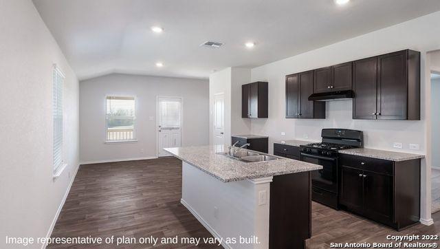 kitchen with sink, dark wood-type flooring, gas stove, a center island with sink, and vaulted ceiling