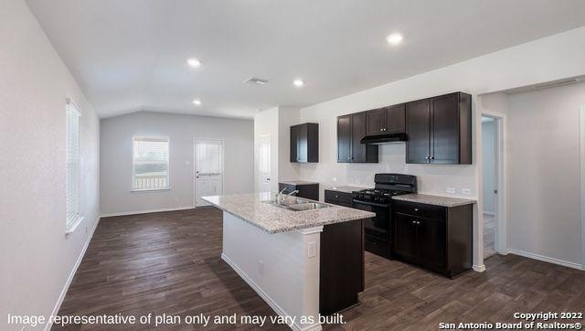 kitchen with sink, black gas range oven, dark hardwood / wood-style flooring, an island with sink, and light stone countertops