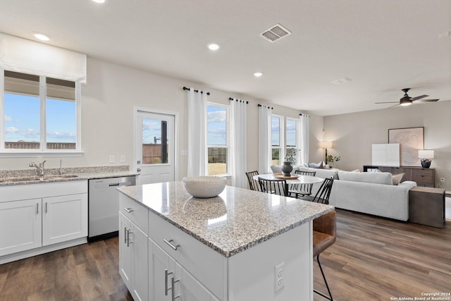 kitchen featuring a kitchen island, sink, white cabinets, stainless steel dishwasher, and light stone counters