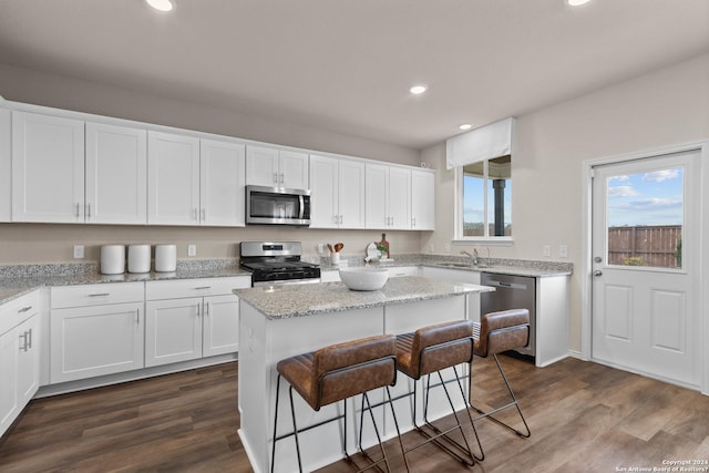 kitchen with appliances with stainless steel finishes, light stone counters, a kitchen island, dark hardwood / wood-style floors, and white cabinetry