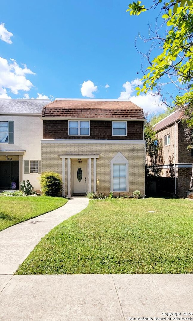 view of front of home with fence, roof with shingles, mansard roof, a front lawn, and brick siding