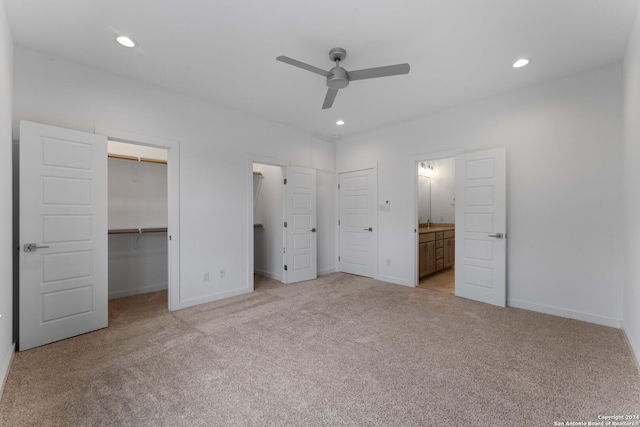 unfurnished bedroom featuring light carpet, ceiling fan, ensuite bath, a walk in closet, and a closet