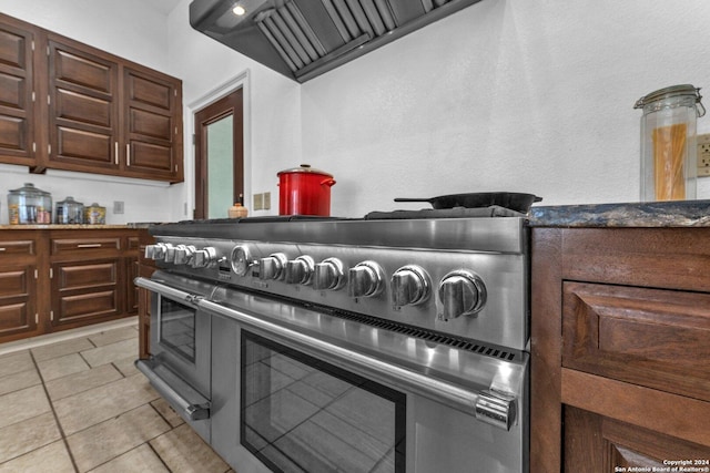 kitchen featuring dark brown cabinets, premium range hood, high end stainless steel range, and light tile patterned flooring