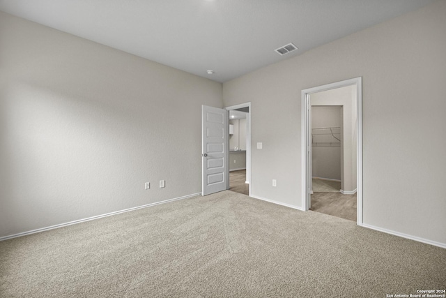 unfurnished bedroom with a walk in closet, a closet, and light colored carpet