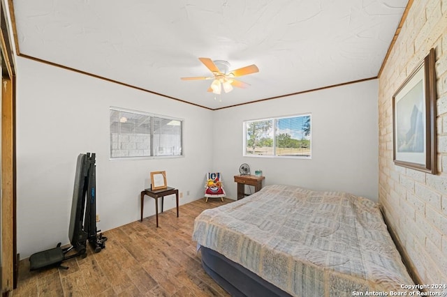 bedroom featuring hardwood / wood-style floors, ceiling fan, crown molding, and brick wall