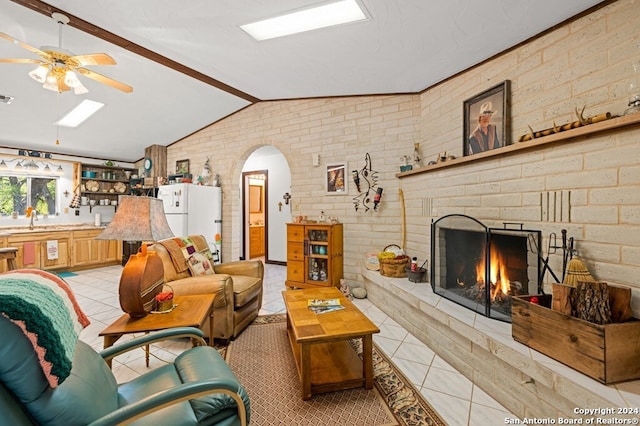 living room with a brick fireplace, brick wall, ceiling fan, light tile patterned floors, and lofted ceiling with beams