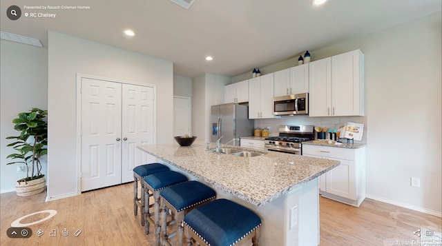 kitchen with light wood-type flooring, stainless steel appliances, a kitchen island with sink, backsplash, and sink